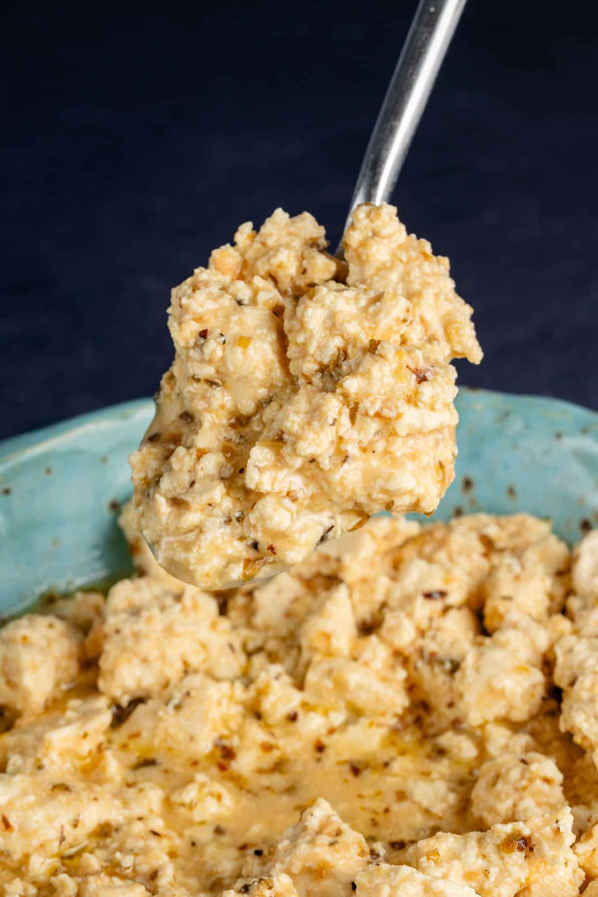 a spoonful of vegan feta cheese lifting out of blue bowl