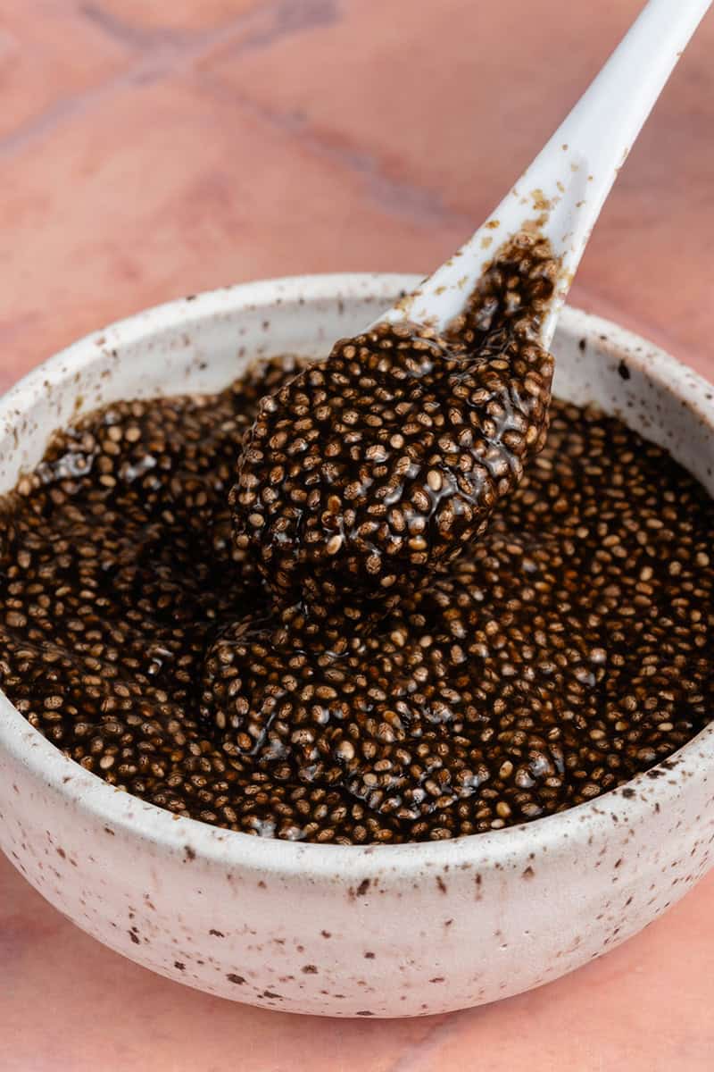 close up of a spoonful of chia seed caviar in a white bowl on a pink background