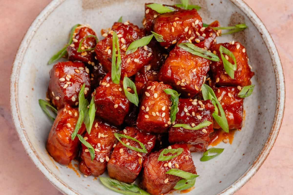 gochujang braised tempeh in a bowl topped with scallions and sesame seeds