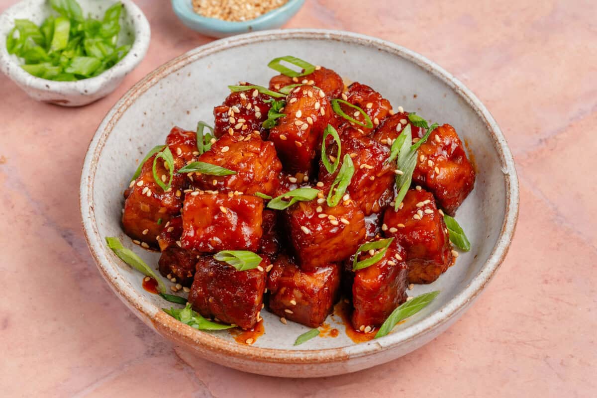 close up of gochujang braised tempeh in a bowl topped with scallions and sesame seeds