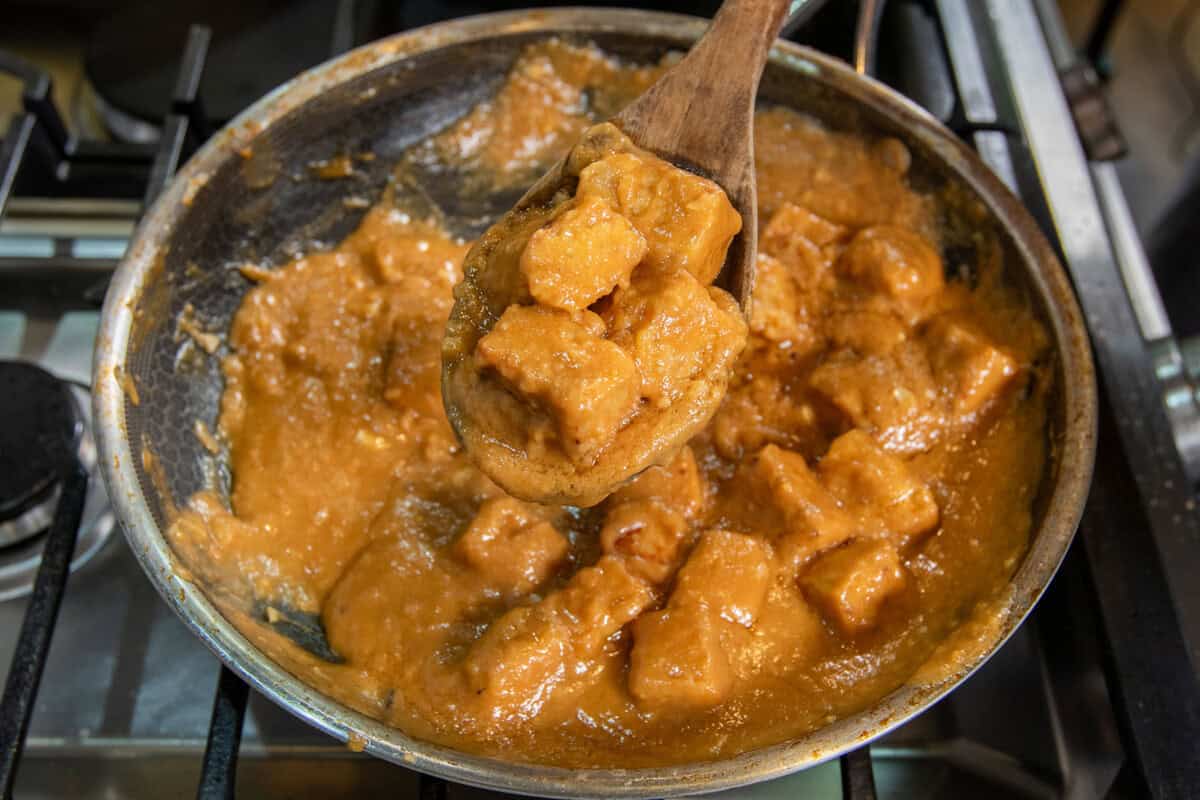 scooping peanut braised tofu out of a pan with wooden spoon