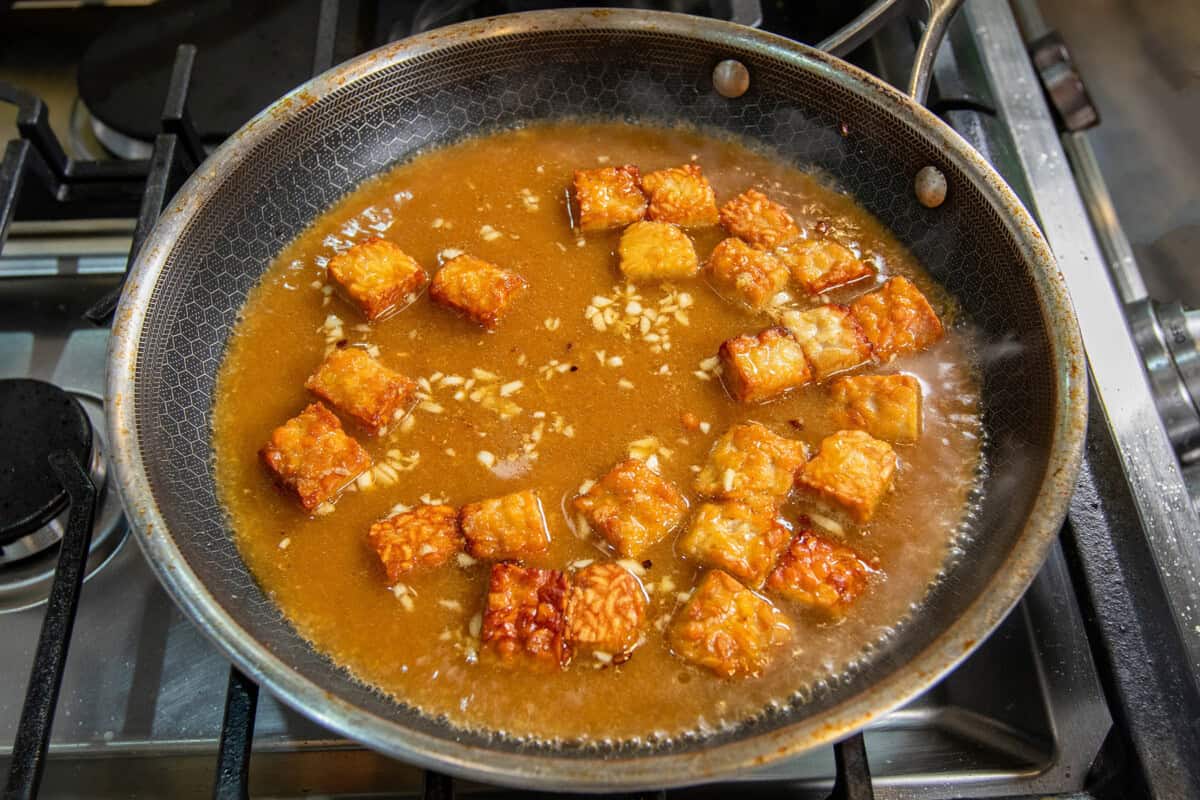 adding sauce to skillet with tempeh