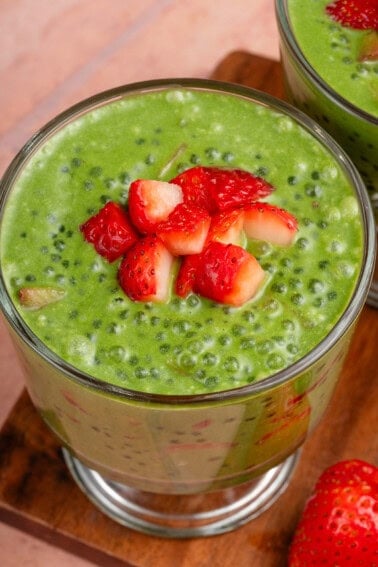 parfait glass filled with strawberry matcha sago and topped with strawberries on wooden board