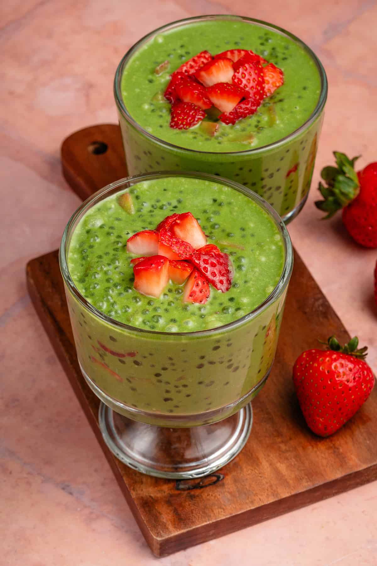 two parfait glasses filled with strawberry matcha sago and topped with strawberries on wooden board