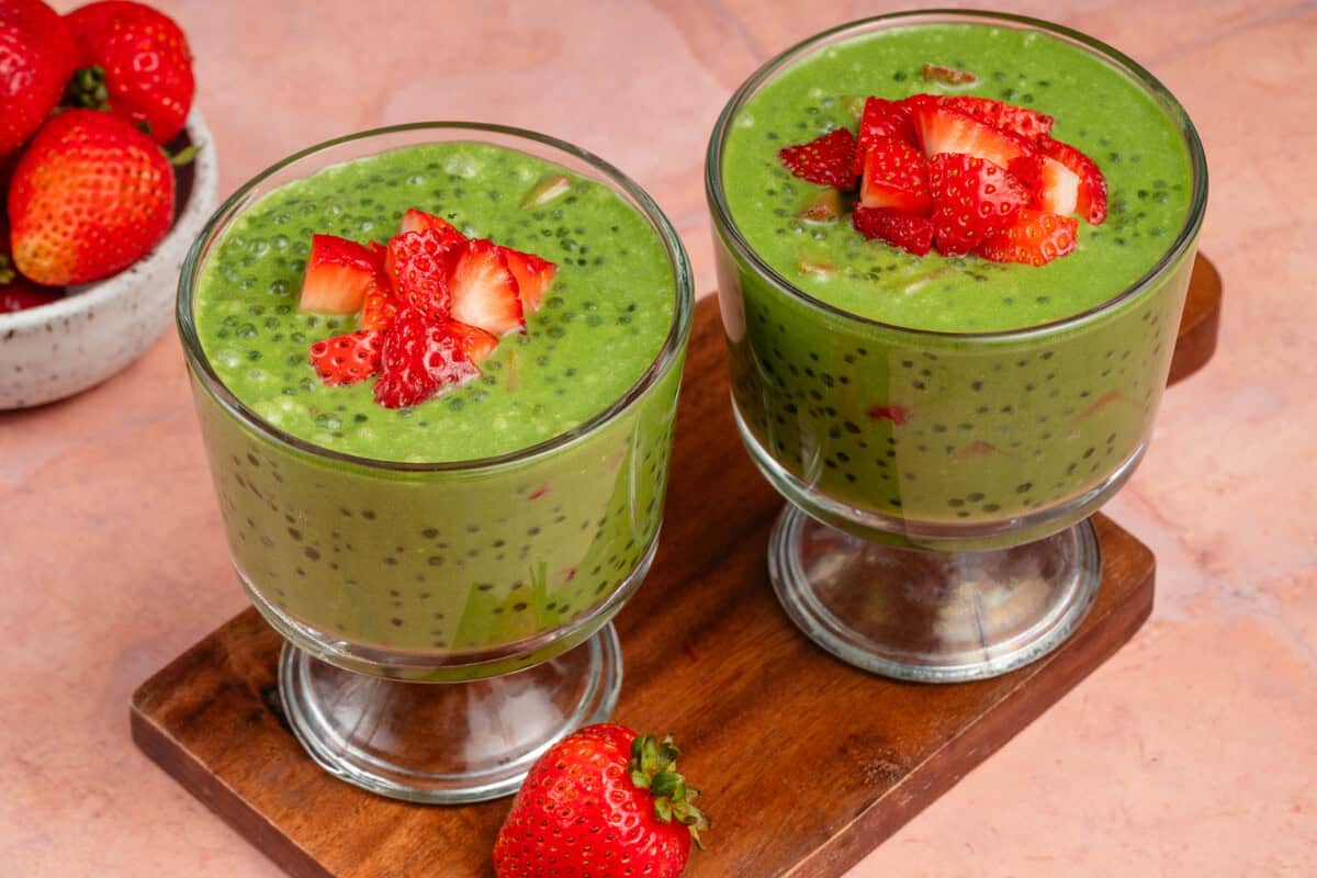 two parfait glasses filled with strawberry matcha sago and topped with strawberries on wooden board
