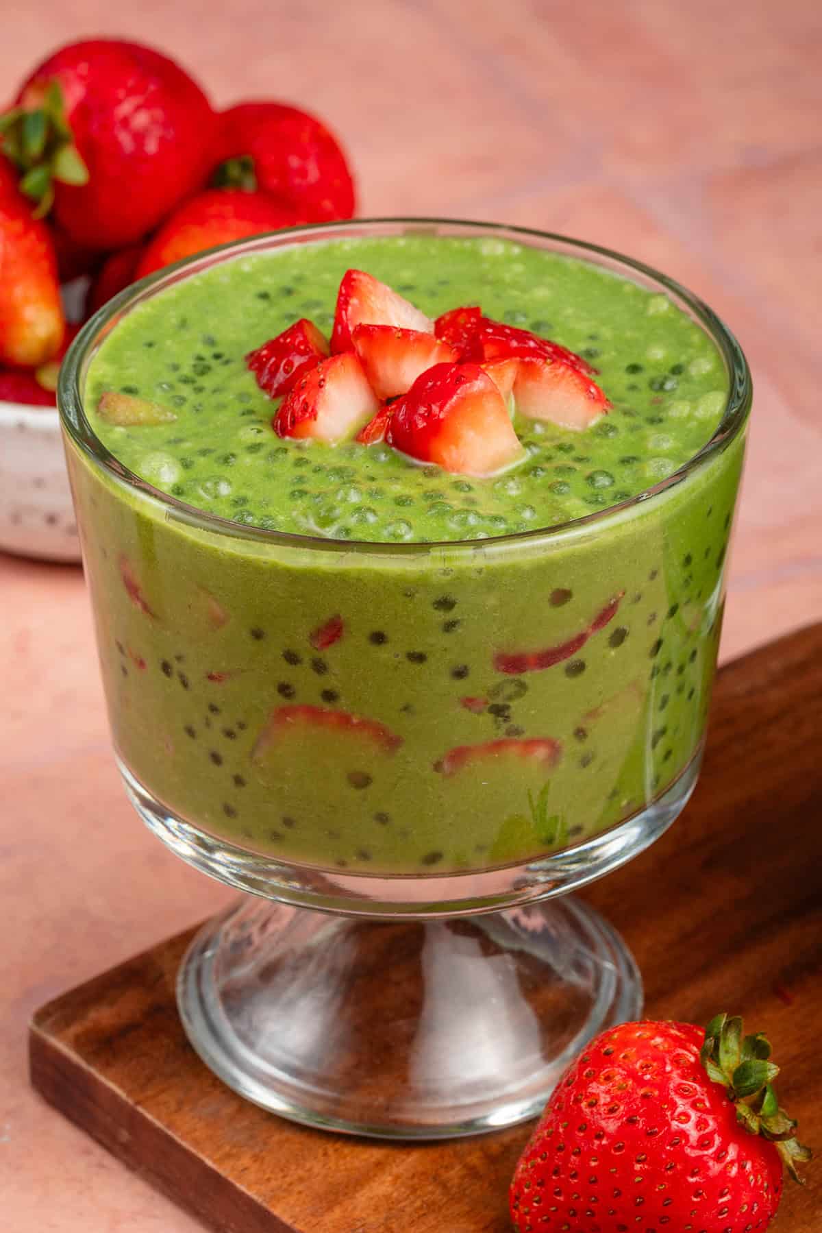 parfait glass filled with strawberry matcha sago and topped with strawberries on wooden board with strawberries in the background