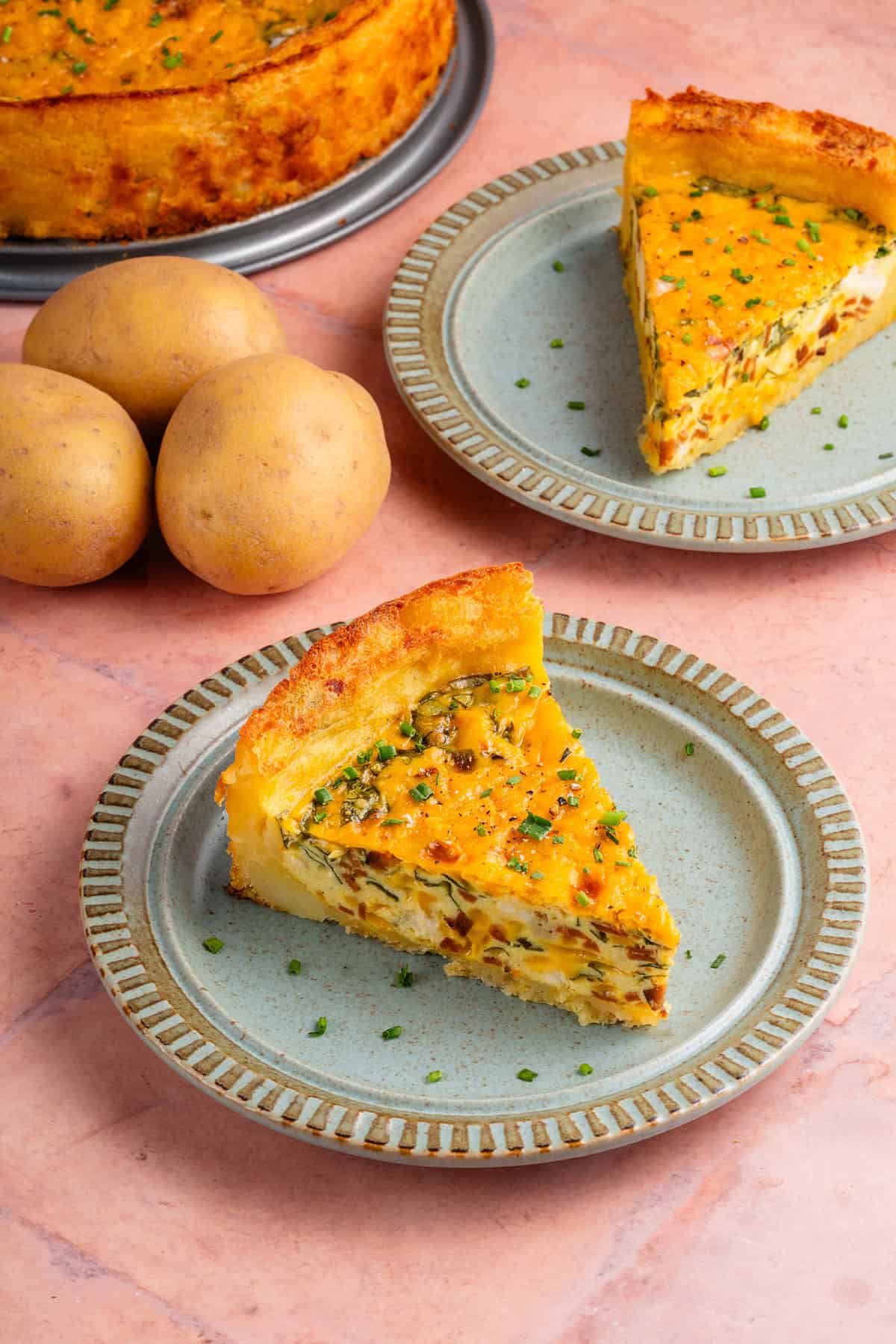 potato crust quiche on a plate with potatoes and another slice in the background
