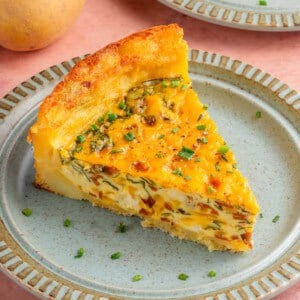 close up of a slice of potato crust quiche on a plate with potatoes and another slice in the background