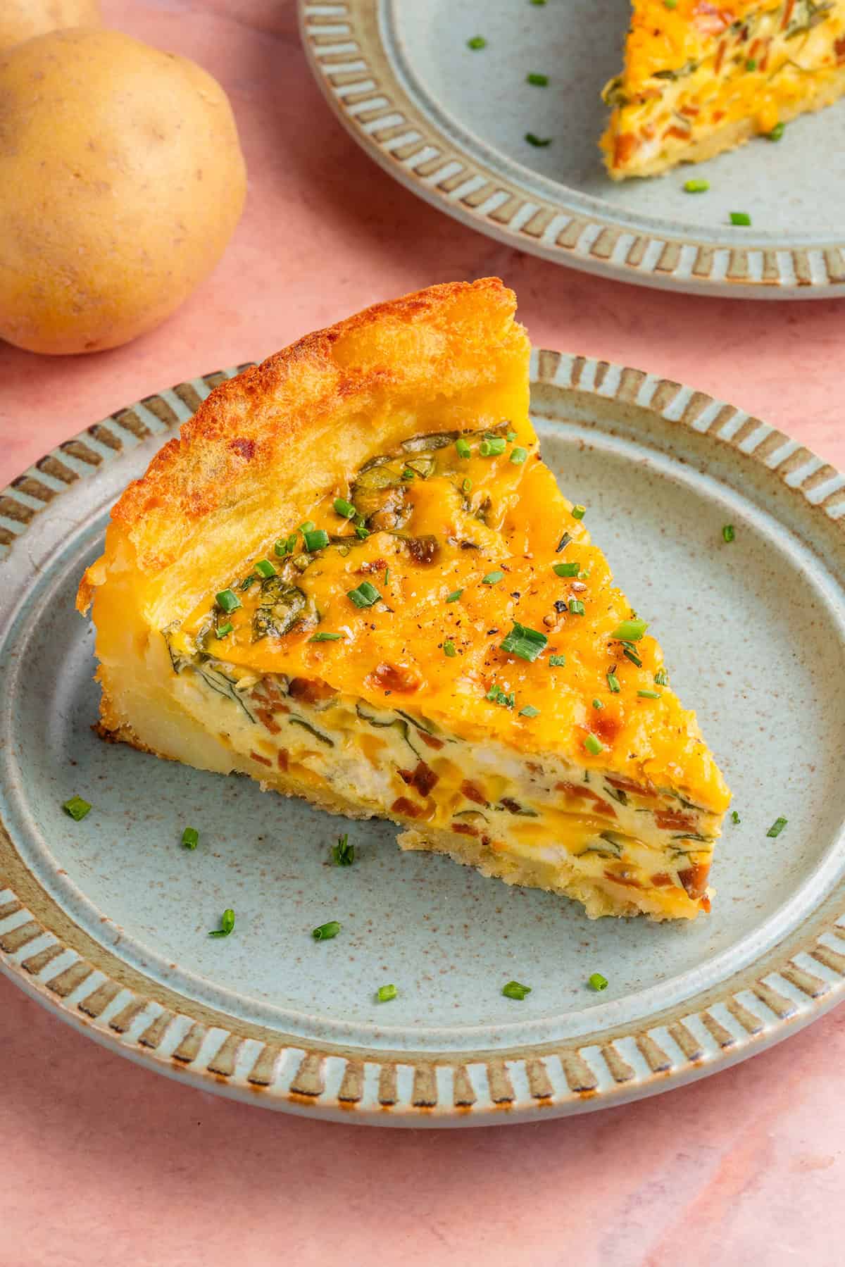 close up of a slice of potato crust quiche on a plate with potatoes and another slice in the background