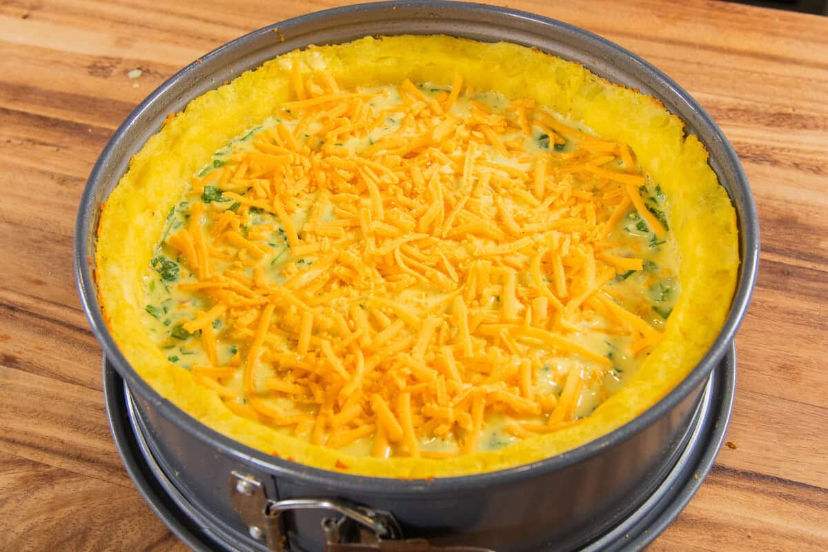potato crust quiche with filling and cheese on top before being baked