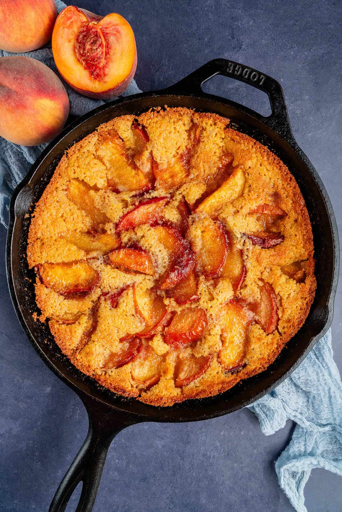 overhead of vegan peach cornbread cobbler in a skillet and peaches on the side
