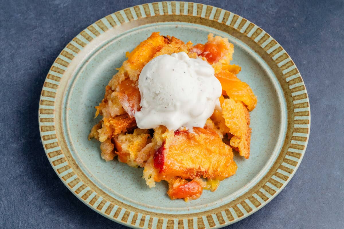 scoop of peach cornbread cobbler on a plate with a vanilla ice cream on top