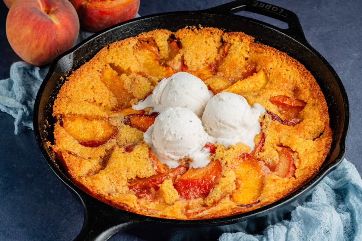 vegan peach cornbread cobbler in a skillet topped with vegan vanilla ice cream