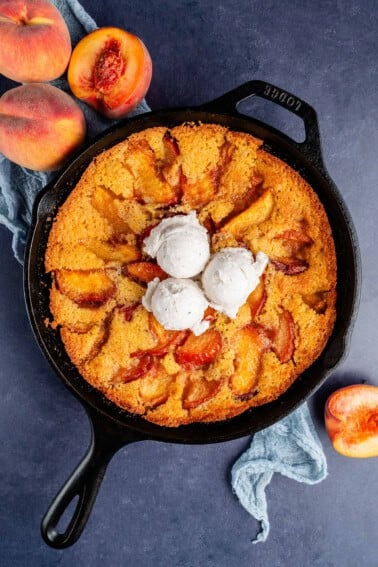 overhead of vegan peach cornbread cobbler with ice cream on top in a skillet and peaches on the side