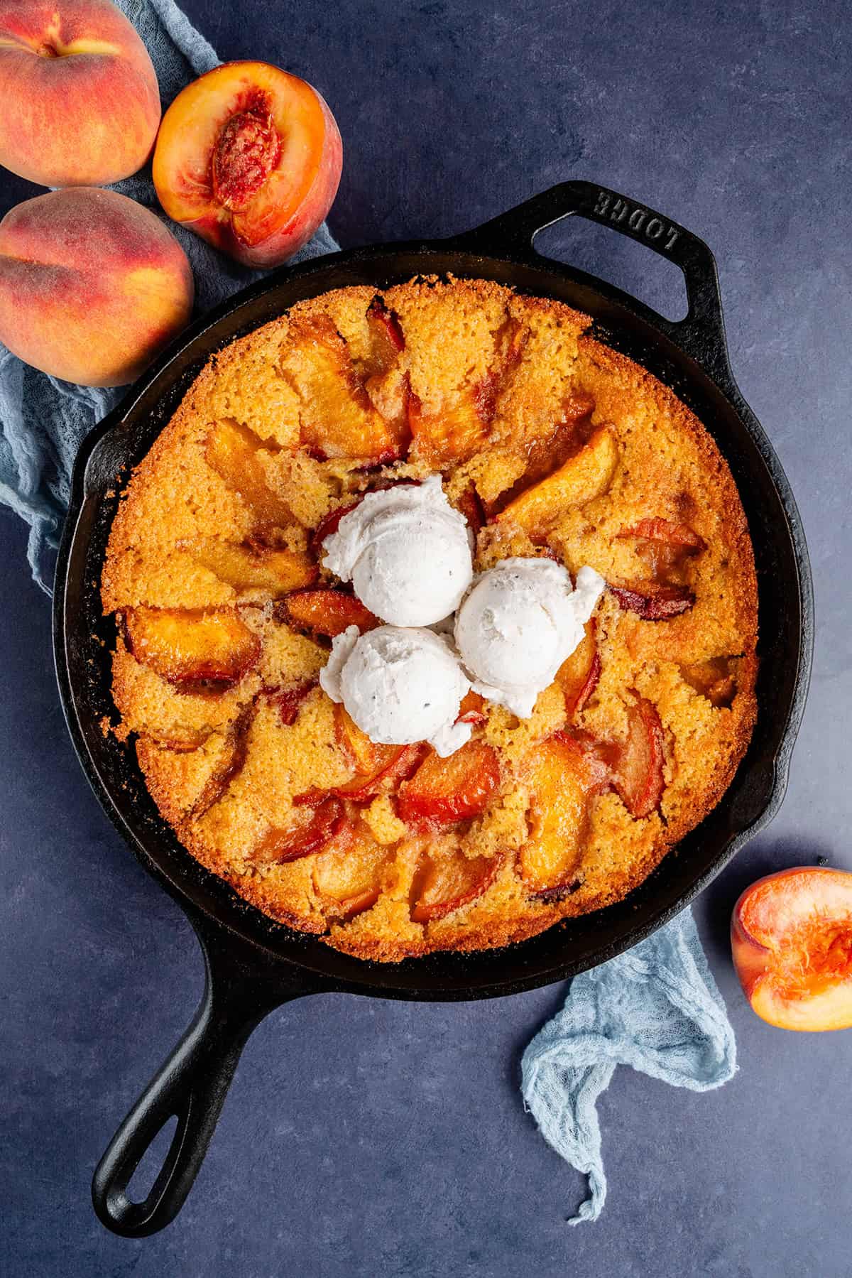 overhead of vegan peach cornbread cobbler with ice cream on top in a skillet and peaches on the side