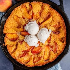 overhead of vegan peach cornbread cobbler with ice cream on top in a skillet and peaches on the side