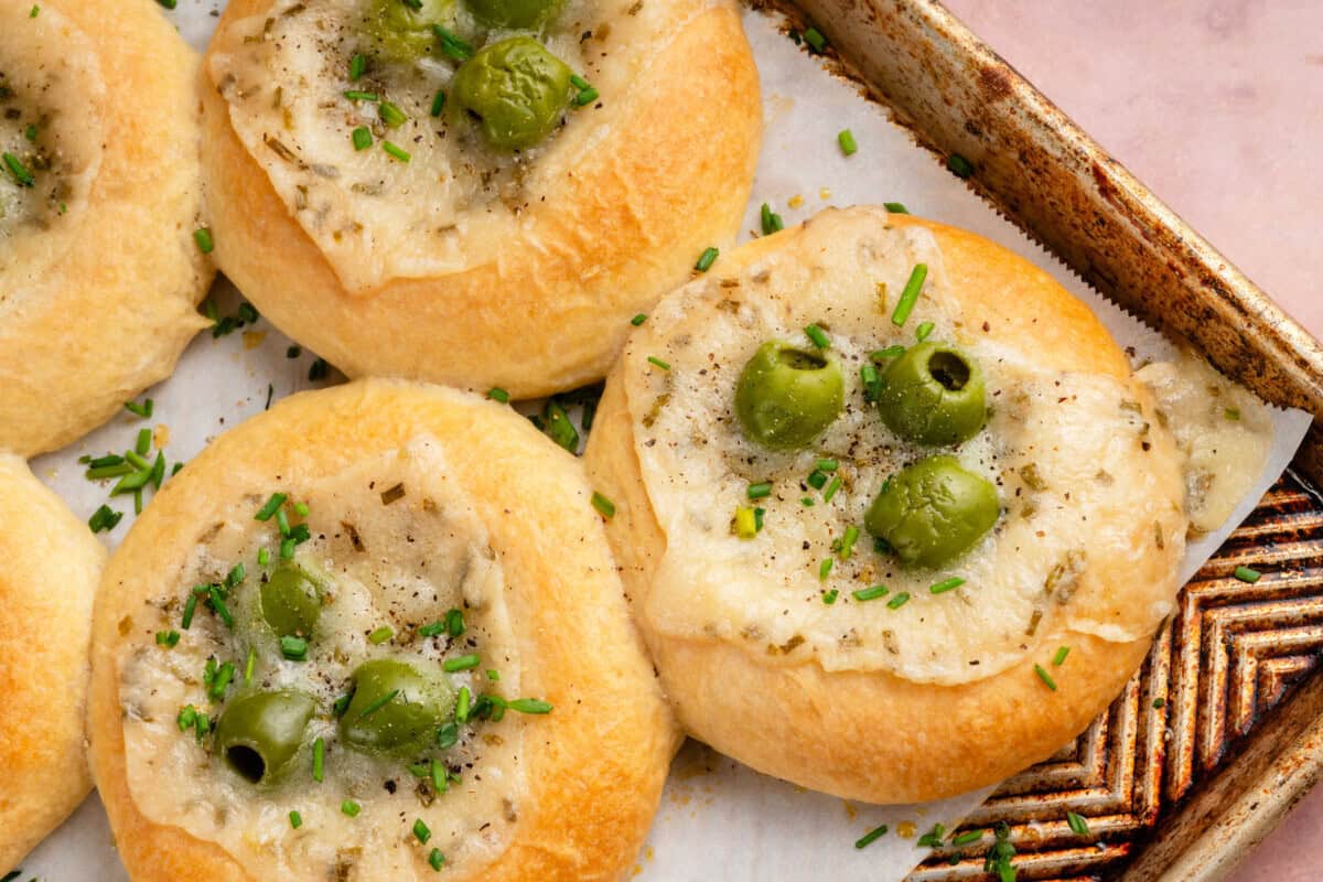 horizontal photo of Olive Chive Cream Cheese Rolls on baking sheet on pink surface