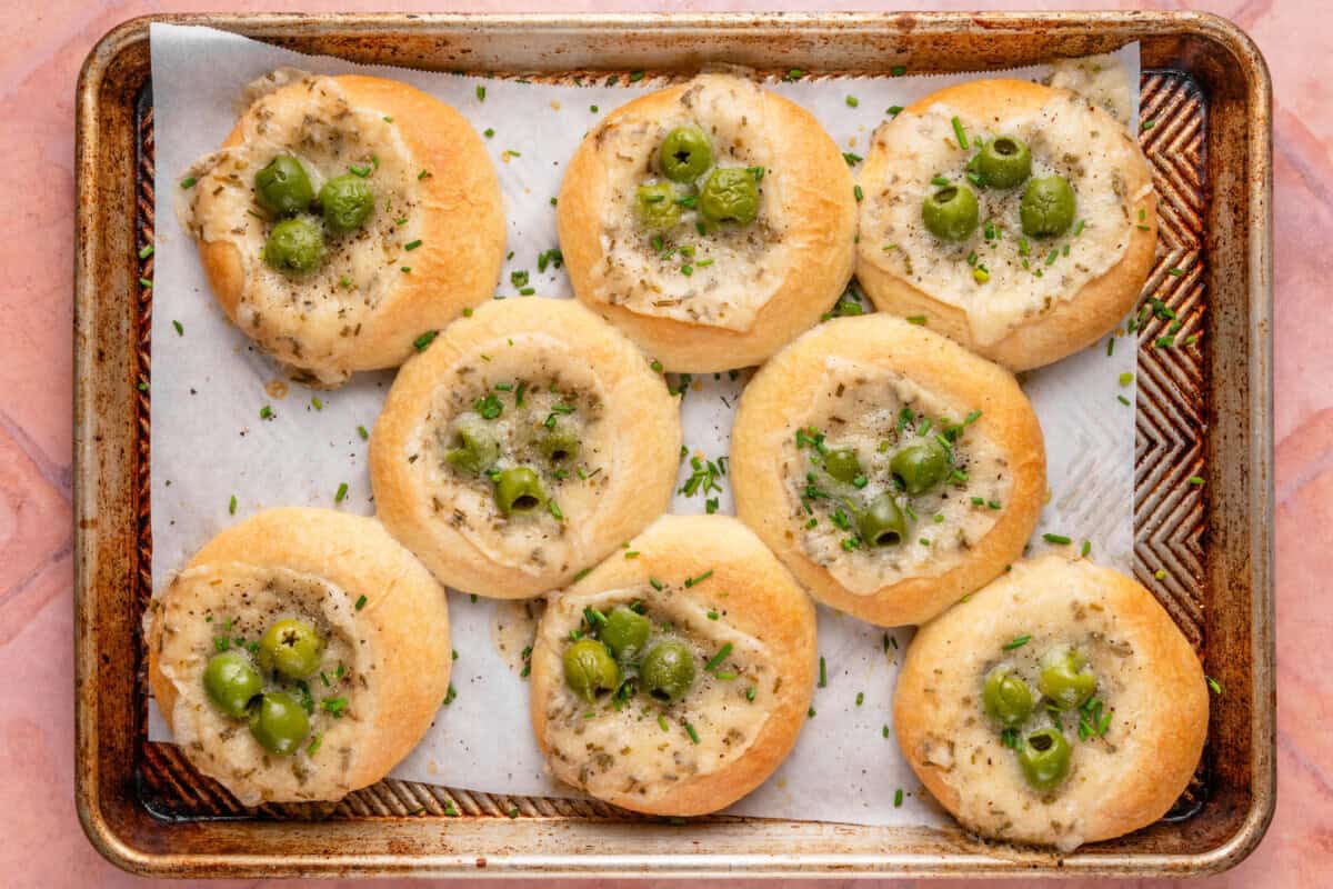 horizontal photo of Olive Chive Cream Cheese Rolls on baking sheet on pink surface