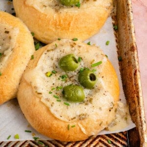 close up photo of a Olive Chive Cream Cheese Roll on baking sheet on pink surface