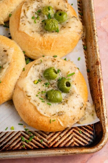 close up photo of a Olive Chive Cream Cheese Roll on baking sheet on pink surface