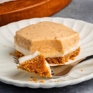 a cut Pumpkin Cheesecake Bar with a fork on a white scalloped plate with additional bars in the background