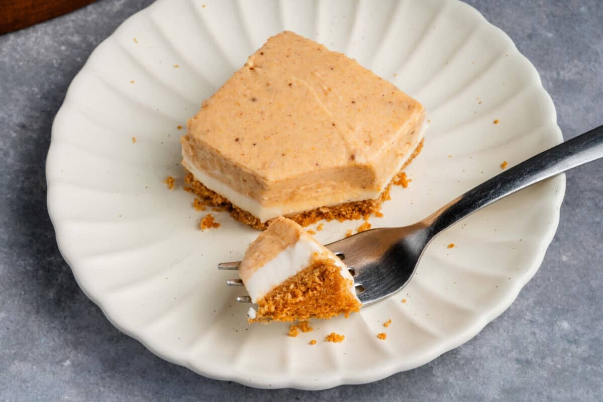 a cut Pumpkin Cheesecake Bar with a fork on a white scalloped plate