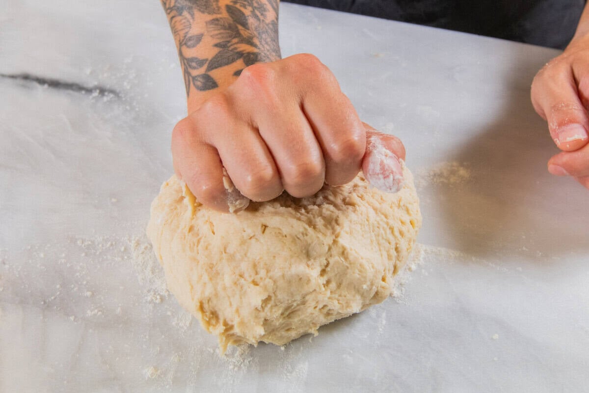 hands kneading dough for Olive Chive Cream Cheese Rolls on white marble surface