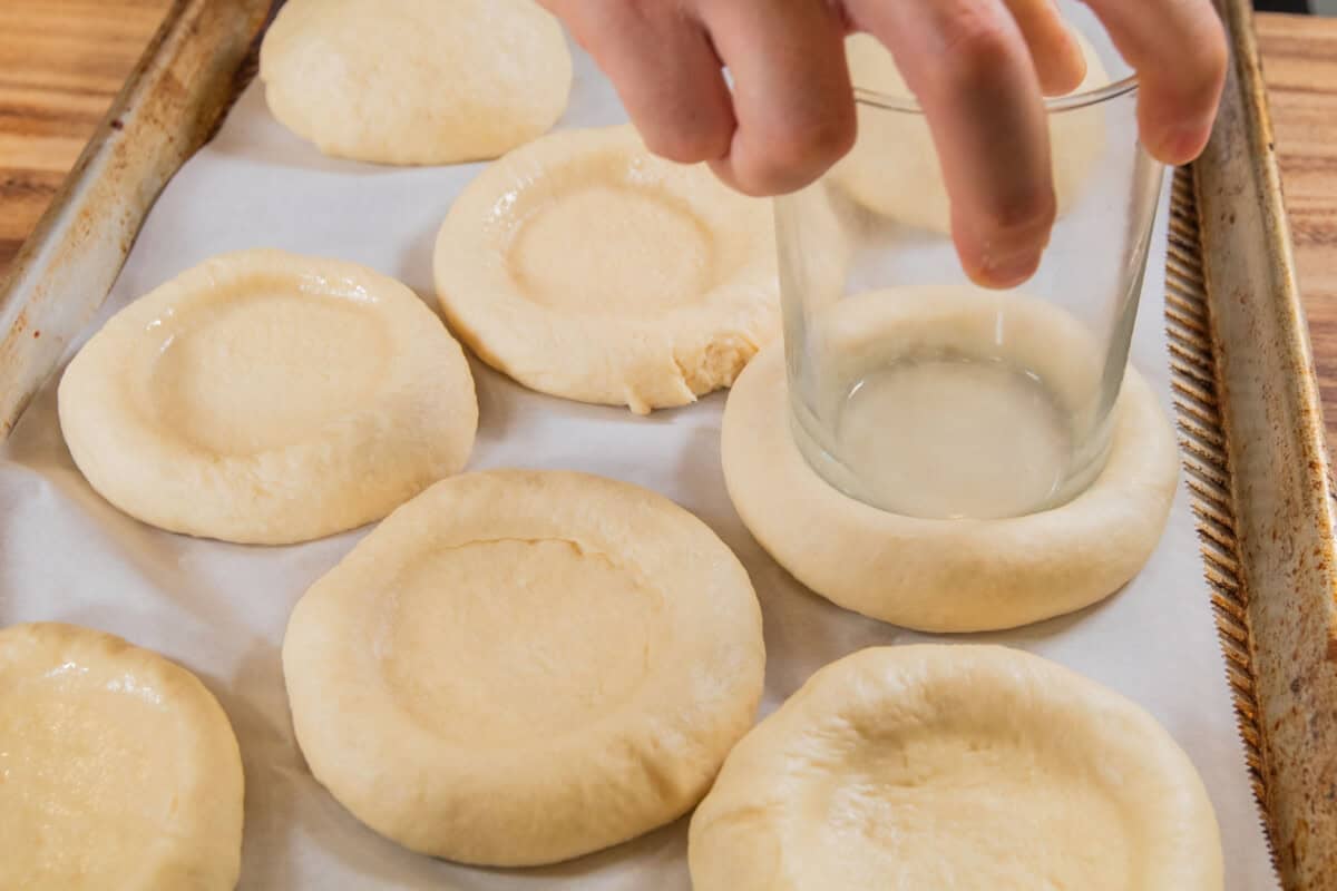 glass cup pressing down into dough balls on baking sheet for Olive Chive Cream Cheese Rolls
