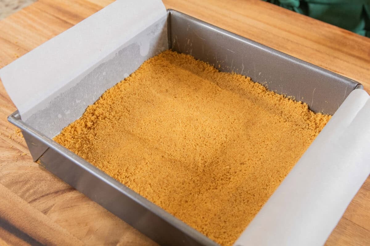 baked graham cracker crust in lined baking dish for pumpkin cheesecake bars recipe
