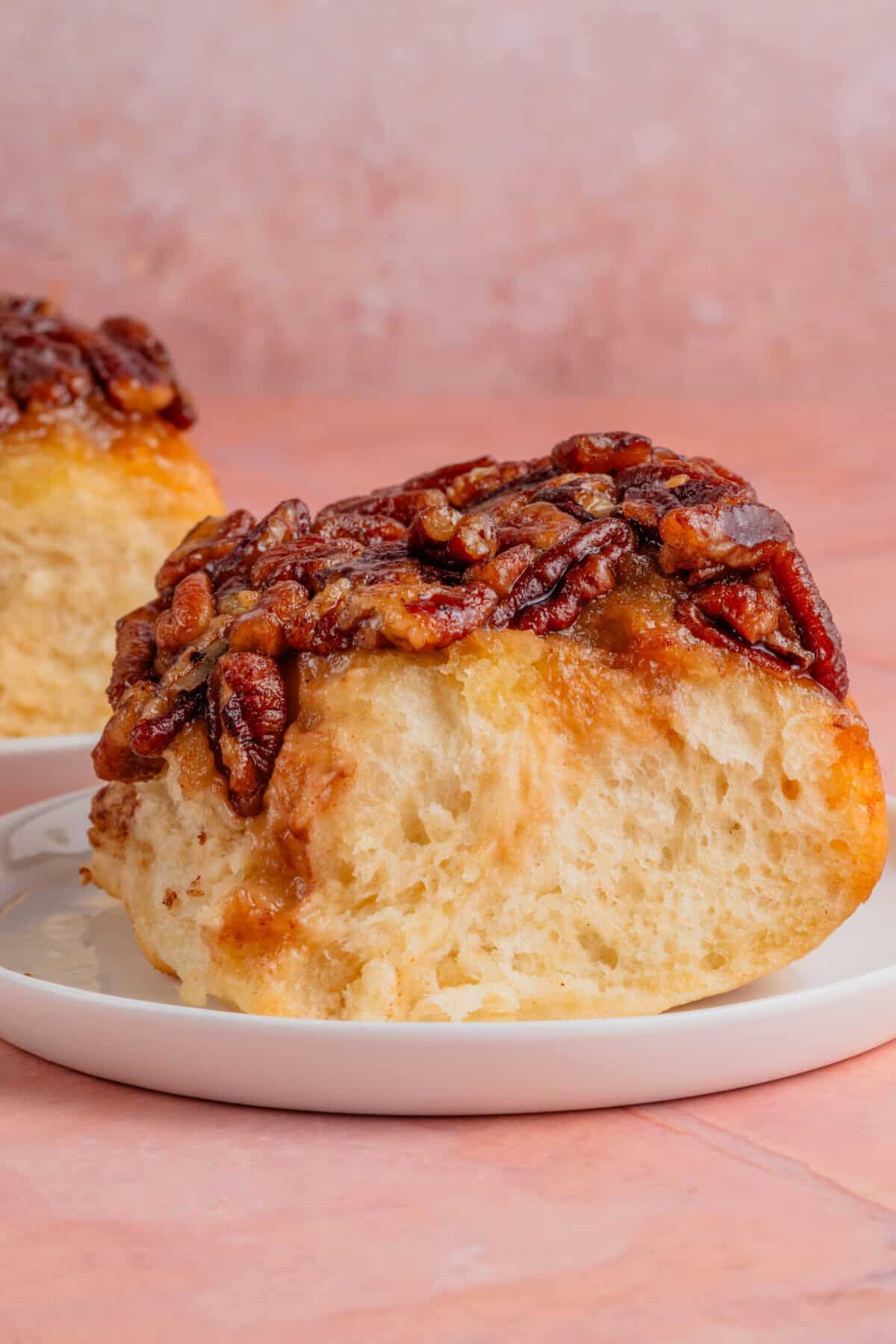 maple pecan sticky buns on a white plate with a pink background
